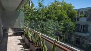 Ein Balkon mit Blumentöpfen und Blick auf eine von Bäumen gesäumte Straße.