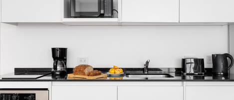 A modern kitchen with white cabinets, a built-in microwave, a coffee maker, a toaster, and a bread loaf on the counter.