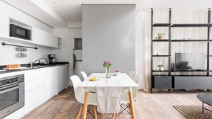 Eine moderne Küche mit weißen Schränken, einer Mikrowelle und einer Kaffeemaschine. Es gibt einen Esstisch mit Stühlen und eine Blumenvase.