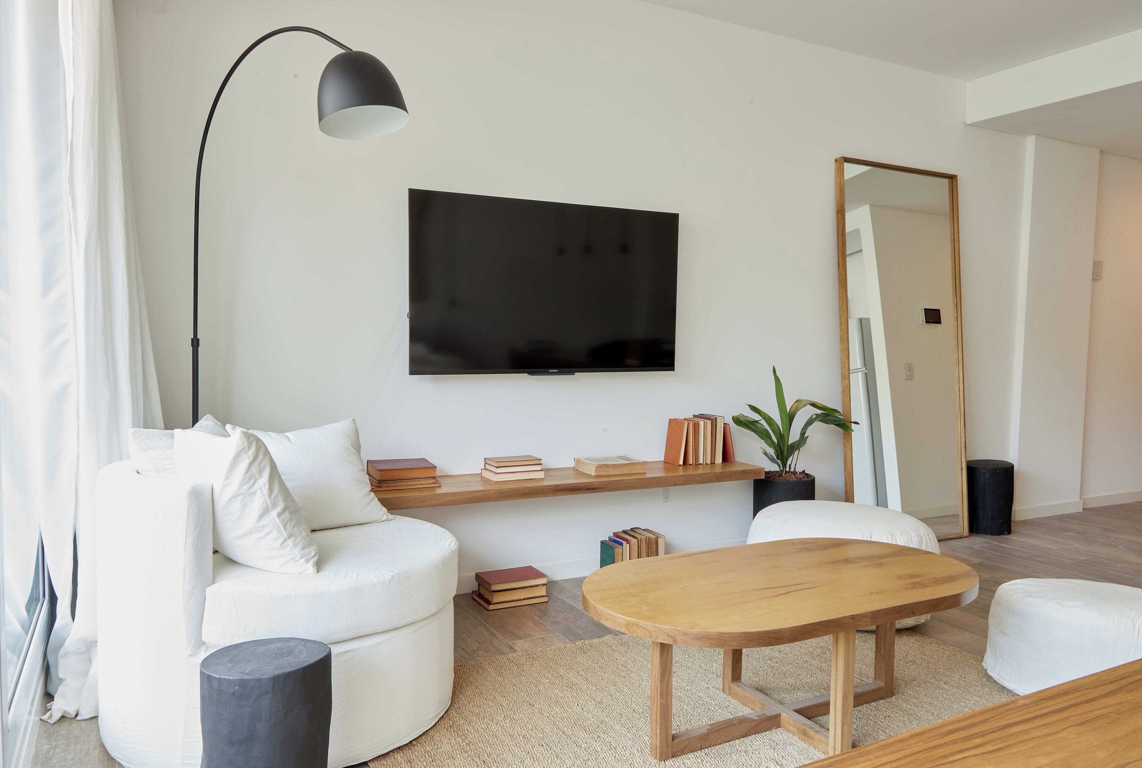 A modern living room with a flat-screen TV, white sofa, wooden coffee table, and a mirror.