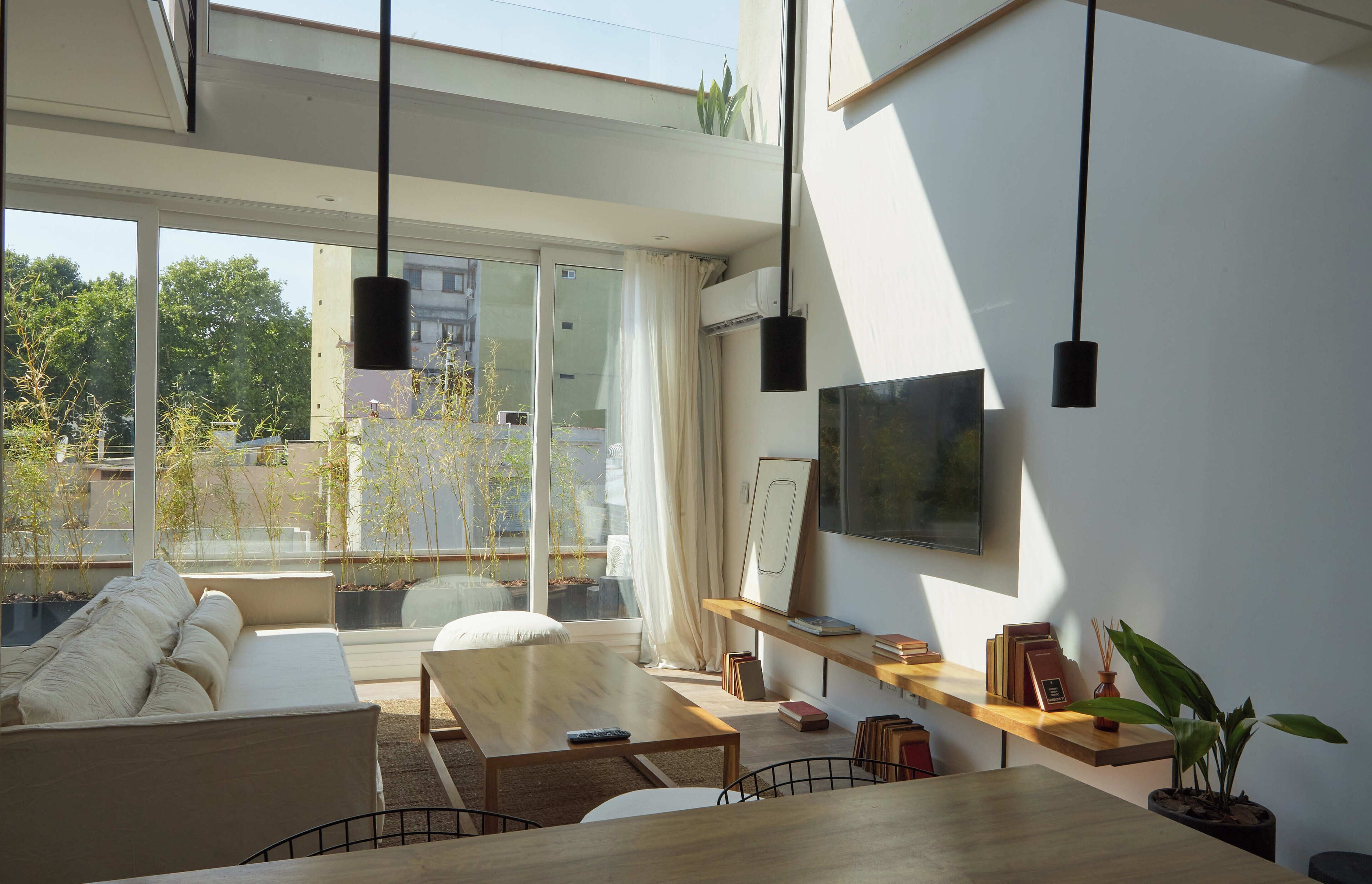 A modern living room with a sofa, a dining table, and a TV mounted on the wall.
