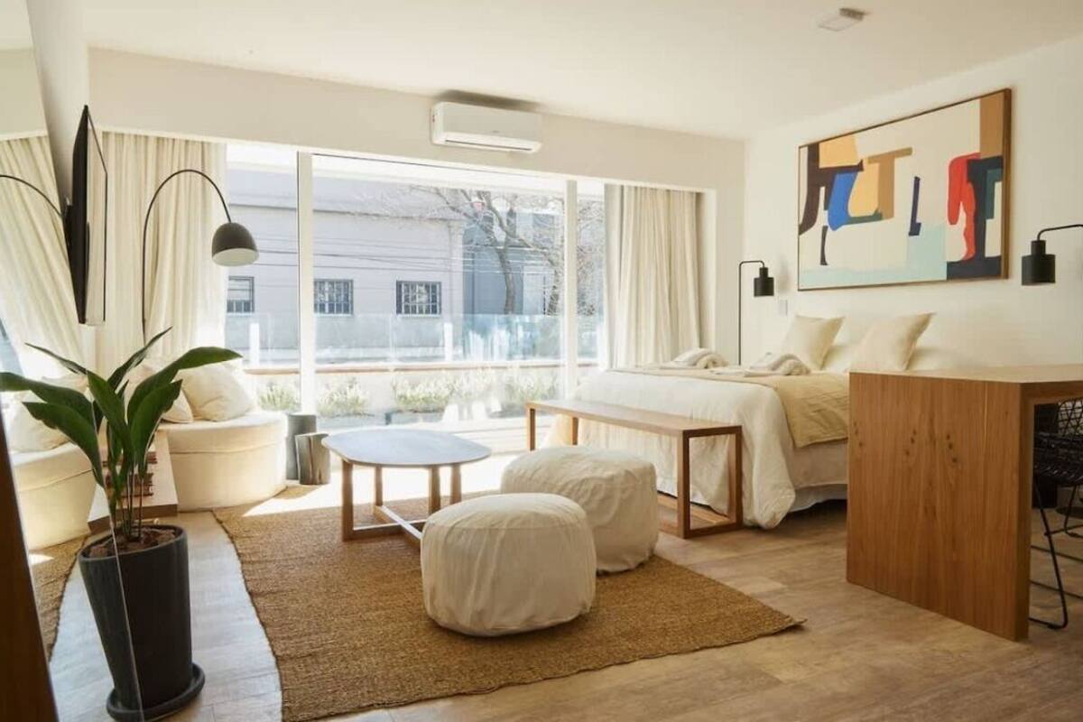 A modern bedroom with a large window, a bed, a desk, and a potted plant.