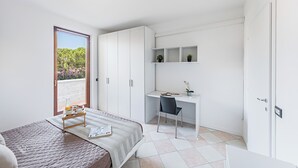 Un dormitorio moderno con cama, escritorio y silla. Se ve un ventanal con vistas a la vegetación.