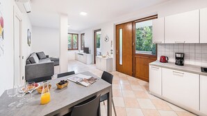 Una cocina moderna con armarios blancos, un comedor con mesa para dos, y una sala de estar con sofá y televisor.