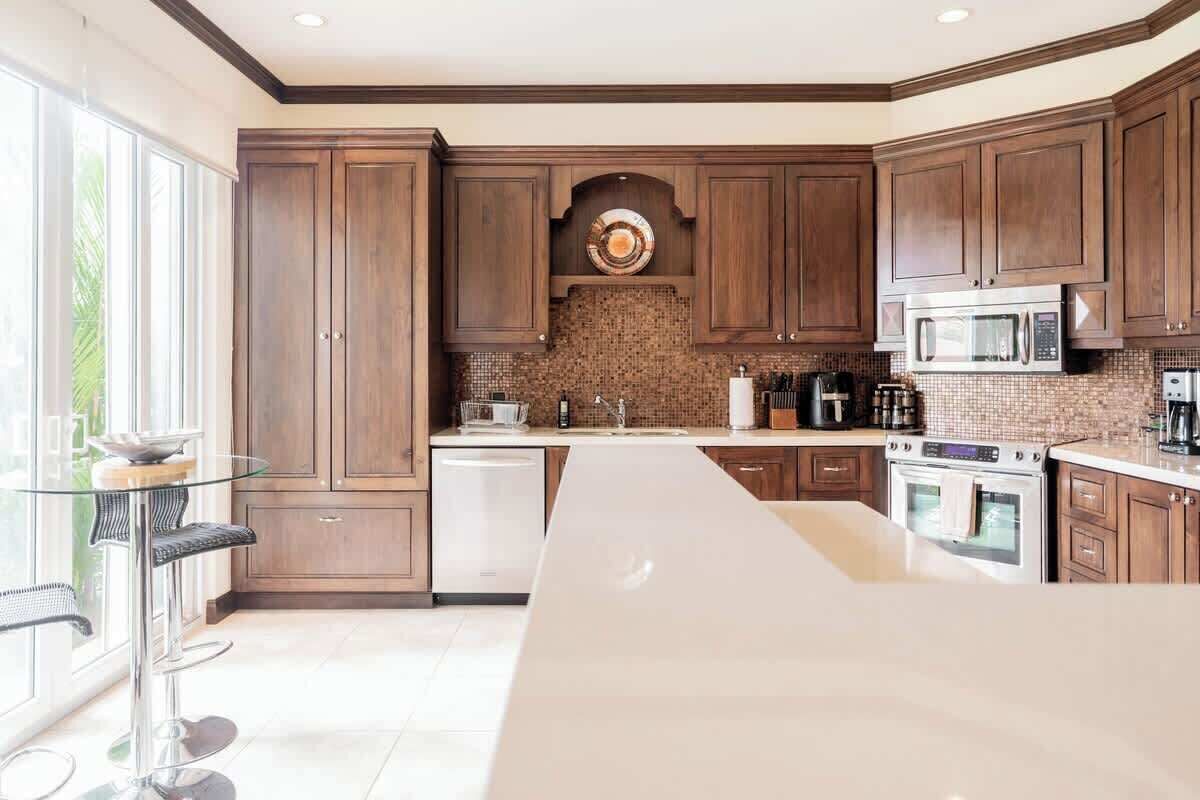 A modern kitchen with dark wooden cabinets, a large island, stainless steel appliances, and a glass bar stool.