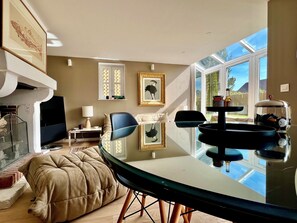 A modern living room with a glass dining table, comfortable seating, a fireplace, and large windows offering a view of the outdoors. - The Duplex at 10 Honfleur (Honfleur)