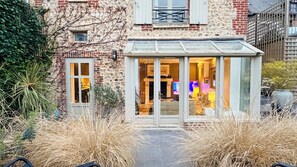 Une véranda dotée d’une porte en verre, un bâtiment en briques et un jardin planté de hautes herbes.
