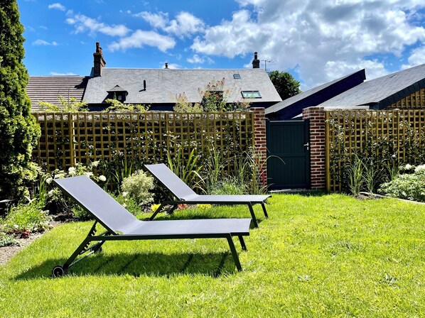 A backyard with two lounge chairs, a wooden fence, and a house with a sloped roof. - The Duplex at 10 Honfleur (Honfleur)