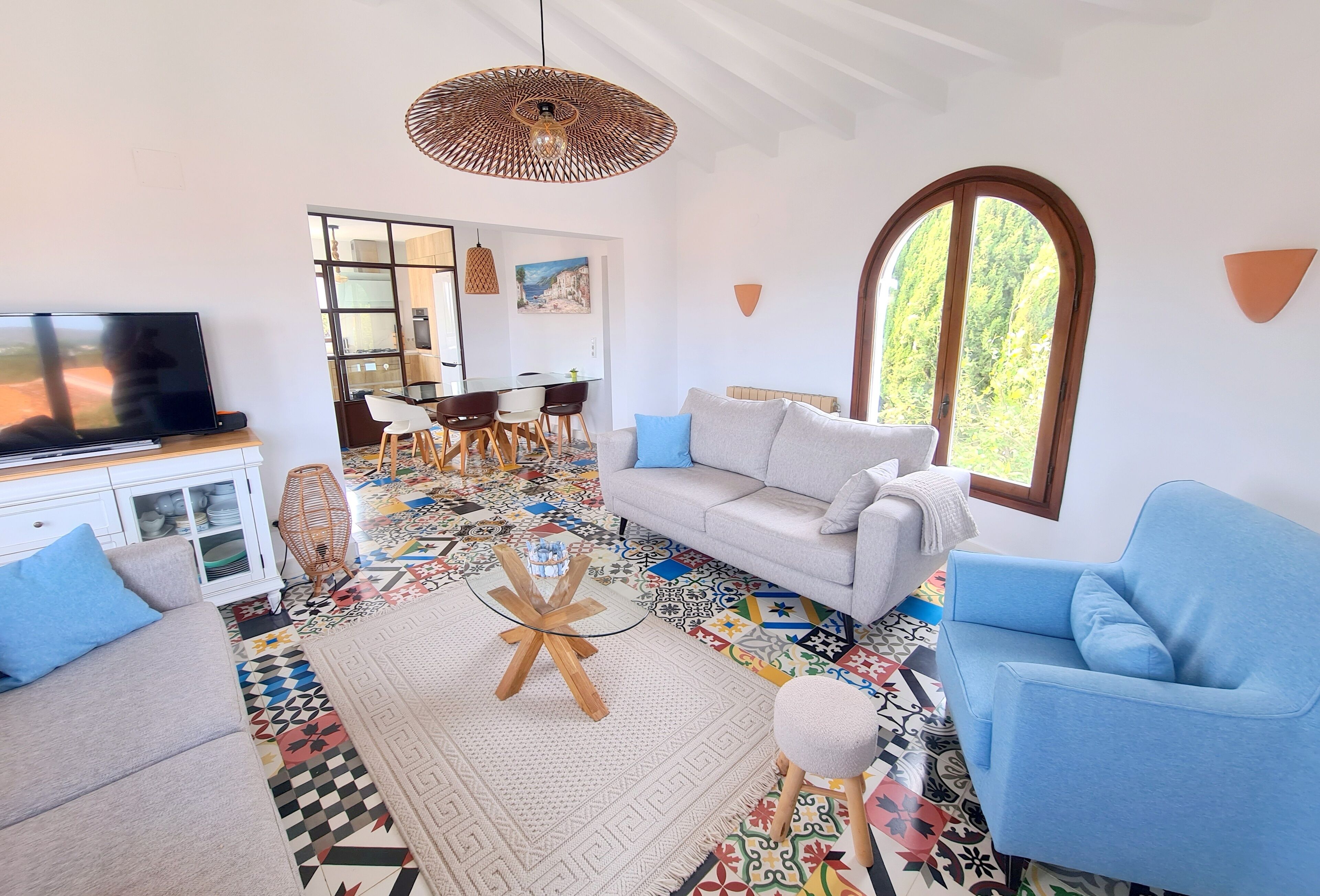 Una sala de estar con sofá, sillón y televisor, un comedor con sillas y mesa, y un suelo con un estampado colorido.