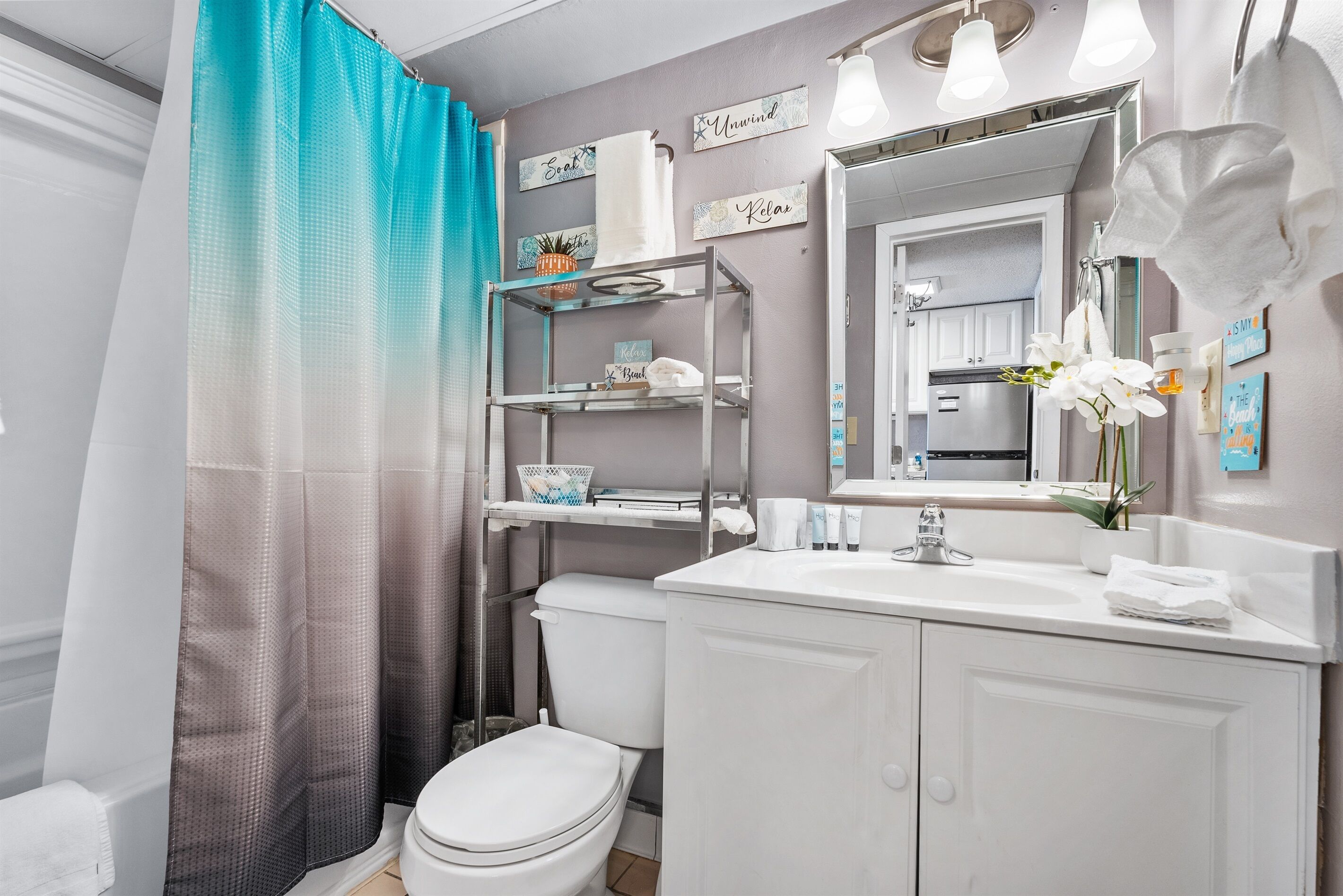 A bathroom with a white toilet, a shower curtain, a sink with a mirror, and shelves with toiletries.