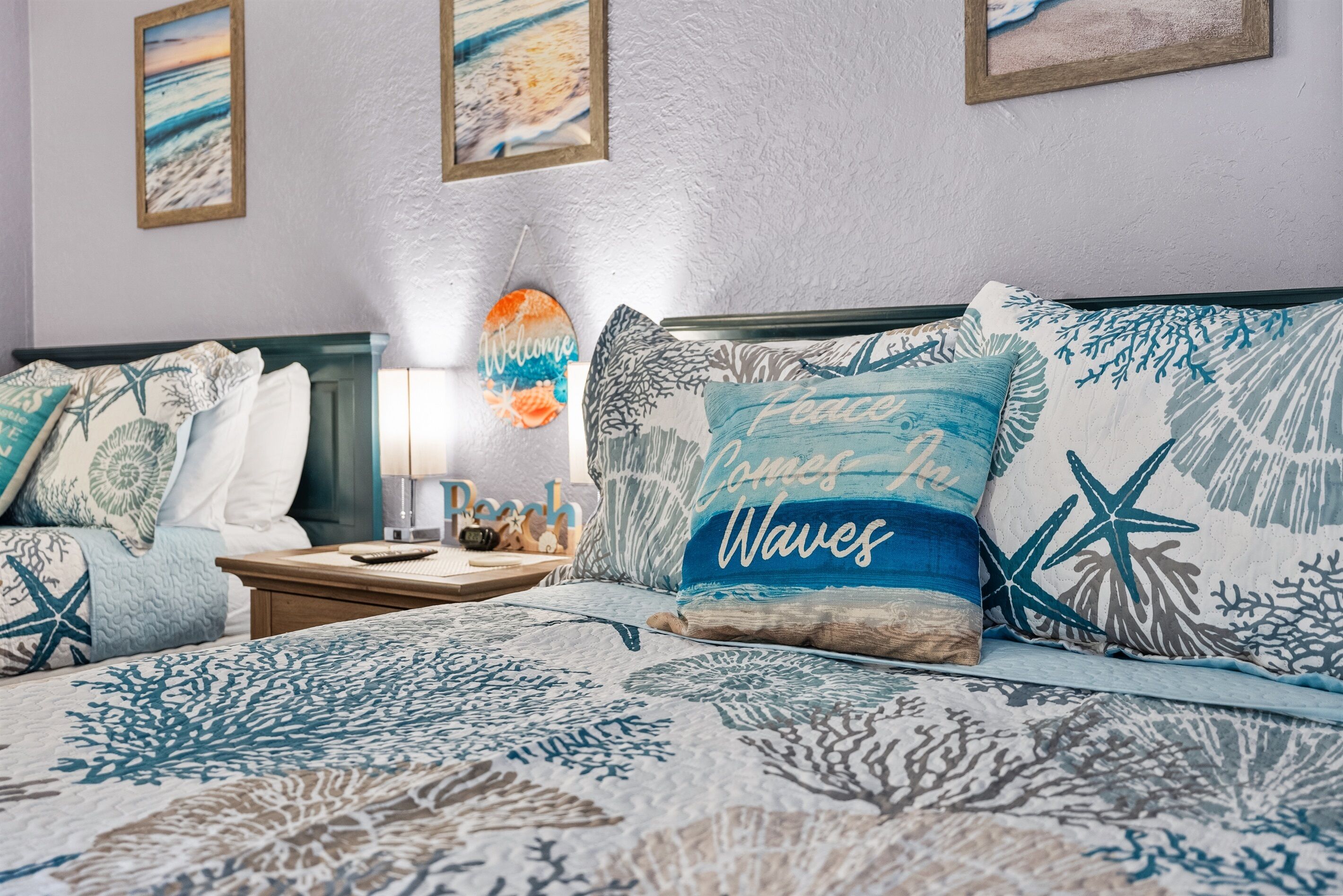 Un dormitorio con cama, cubrecolchón con motivos marinos en azul y blanco, almohadas con diseños náuticos y cuadros en las paredes.