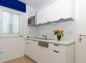 Kitchen features a dishwasher, stainless steel microwave, and a window with blinds.