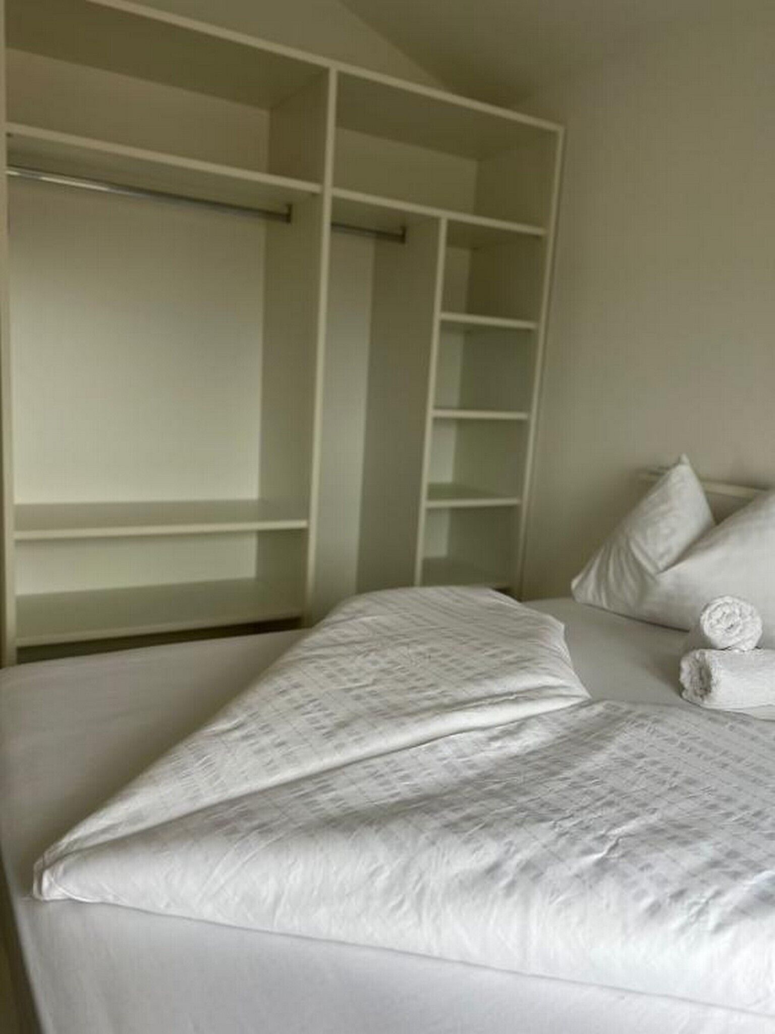 A bedroom with a bed, a built-in wardrobe, and a neatly made bed with rolled towels.
