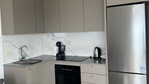 A compact kitchen with a built-in dishwasher, a stainless steel refrigerator, and a marble backsplash.