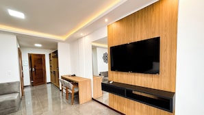 A modern living room with a flat-screen TV mounted on a wooden wall, a wooden desk with a chair, a sofa, and a coffee table. - Aloha Palace (Jijoca de Jericoacoara)