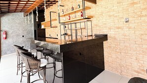 A bar area with a brick wall, wooden ceiling beams, and a bar counter with stools. - Aloha Palace (Jijoca de Jericoacoara)