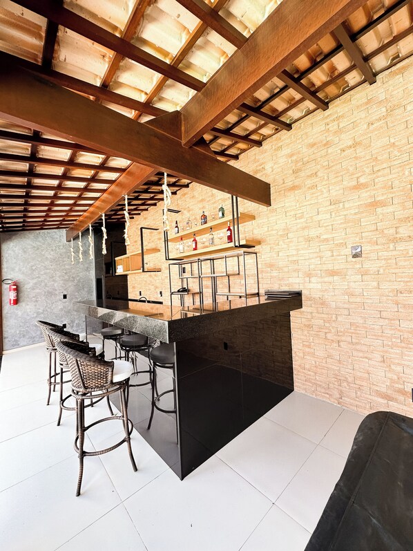 Zona de bar con pared de ladrillo, vigas de madera en el techo y una barra con taburetes.