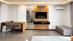 A modern living room with a wooden accent wall, a flat-screen TV, a sofa, a dining area with chairs, and a small kitchen area. - Aloha Palace (Jijoca de Jericoacoara)