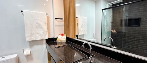 Un baño moderno con lavamanos de mármol negro, cabina de ducha de vidrio y pared revestida de paneles de madera.