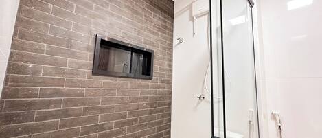 A modern bathroom with a glass shower enclosure, a visible toilet, and a small window.