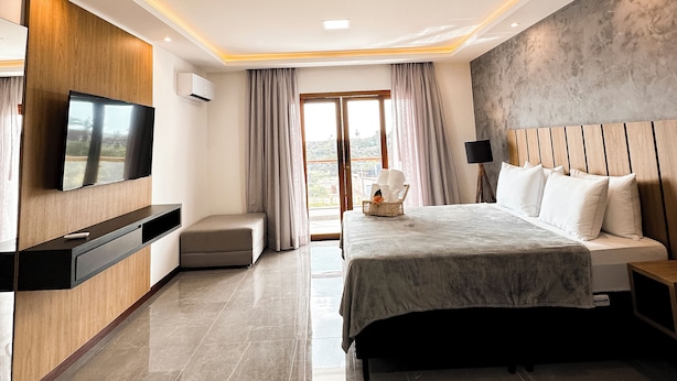 A modern bedroom with a large bed, a TV mounted on the wall, and a balcony with curtains. - Aloha Palace (Jijoca de Jericoacoara)