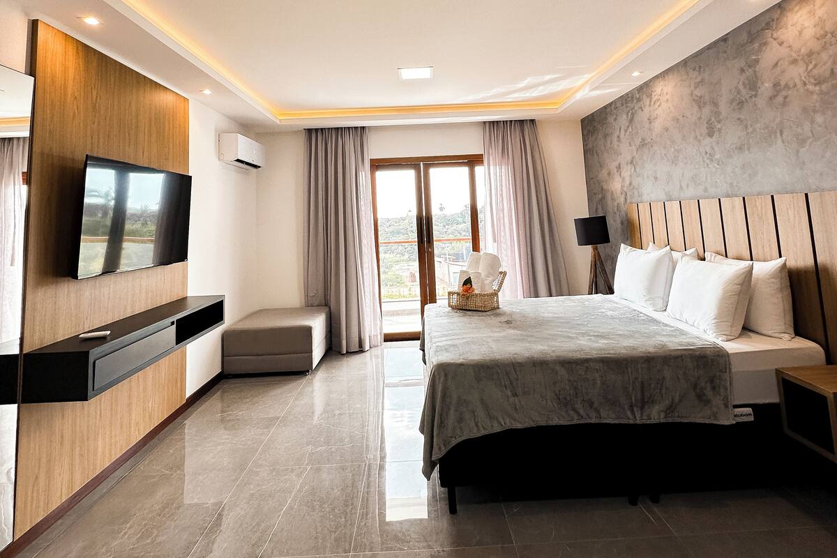 A modern bedroom with a large bed, a TV mounted on the wall, and a balcony with curtains.