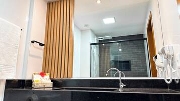 Un bagno moderno con un piano lavabo nero, una parete rivestita in legno e uno spazio doccia in vetro. Un asciugacapelli è montato sulla parete.