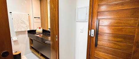 A modern bathroom with a wooden door, a towel rack, a sink with a mirror, and a small trash bin.