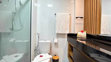 A modern bathroom with a glass shower enclosure, a toilet with a white lid, and a black trash bin.