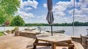 An outdoor patio with a wooden table and benches, a stone wall, and a view of a lake with boats. - Lakefront Vacation Rental ~ 10 Mi to Shipshewana! (Howe)