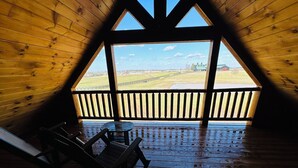 Eine Holzhütte mit geneigtem Dach und Blick auf eine grüne Landschaft durch ein großes Fenster.