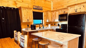 Ein Holzblockhaus-Innenraum mit einer Küche, die eine große Kochinsel, Barhocker und ein Schild mit der Aufschrift 'Kentucky Derby' zeigt.