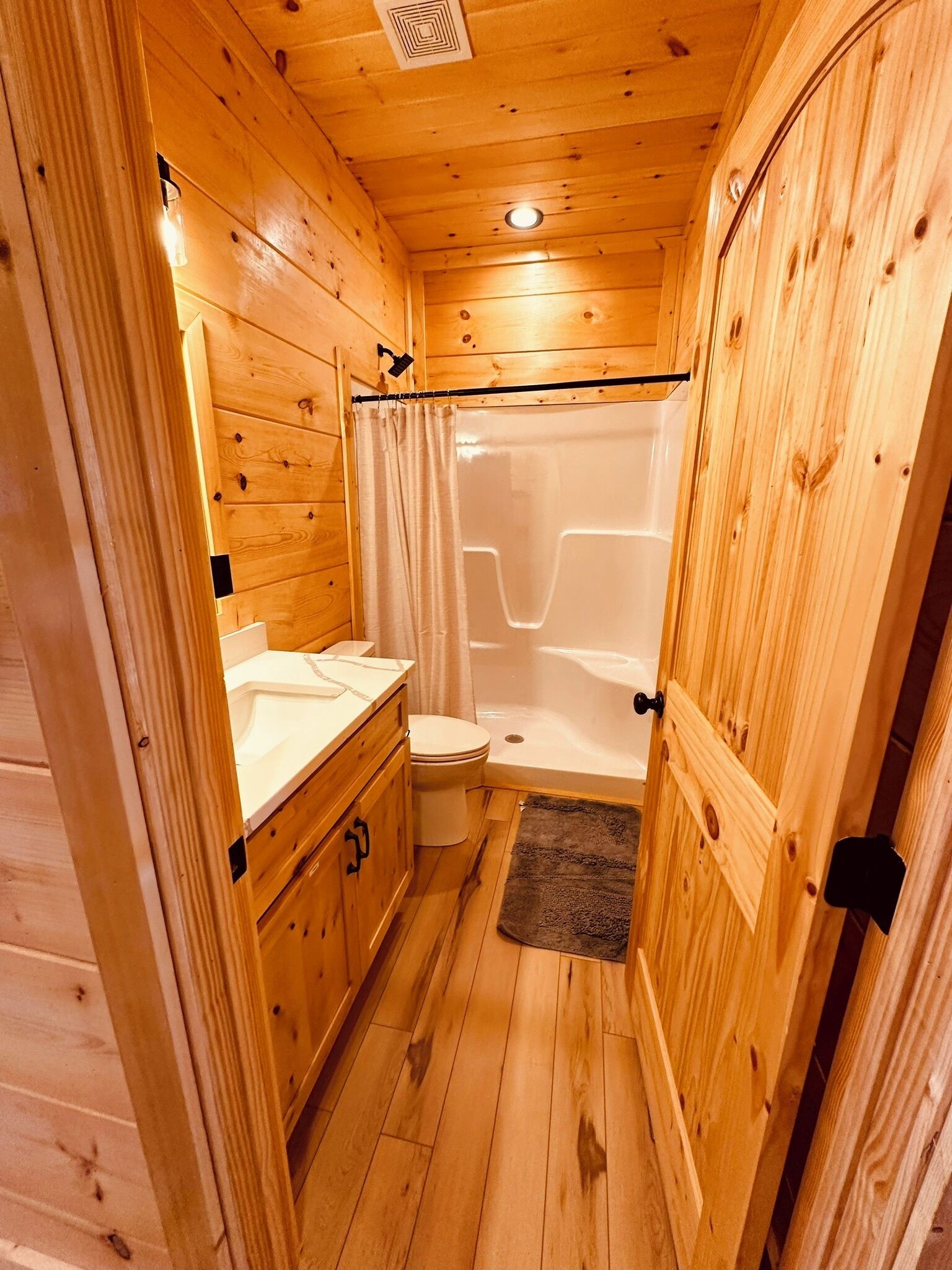 A wooden cabin bathroom with a shower, toilet, and vanity.