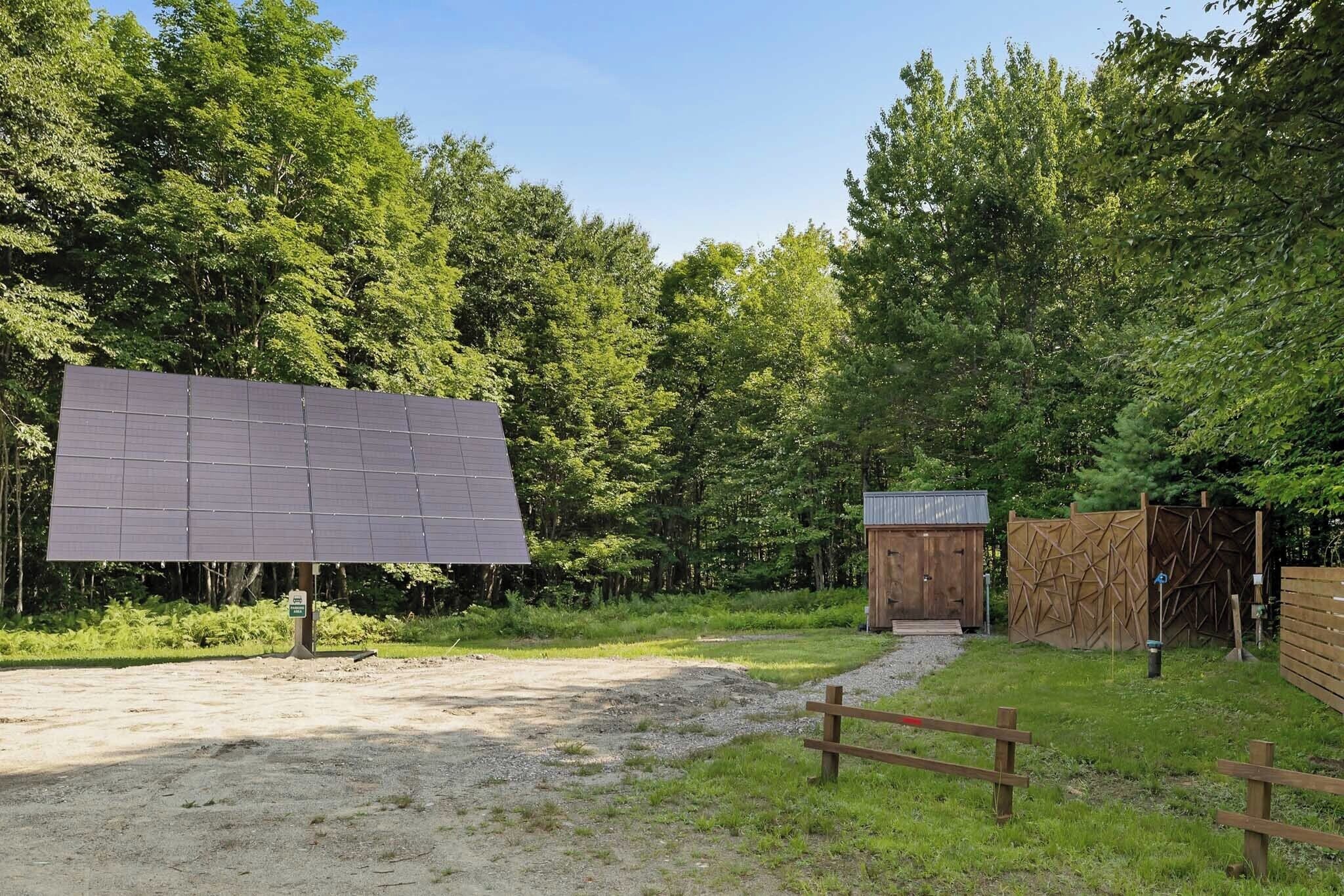 A solar panel installation in a wooded area with a small wooden structure nearby.