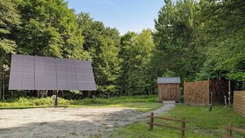 A solar panel installation in a wooded area with a small wooden structure nearby.