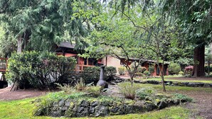 A garden with a stone pathway, a wooden gazebo, and a red building with a sloped roof.