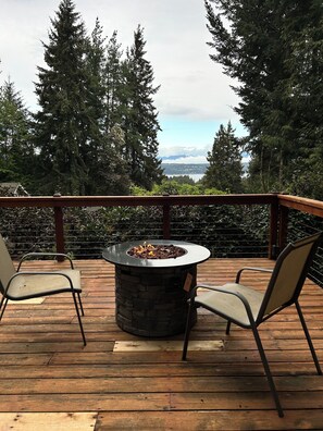 Eine Terrasse mit einem Steinkamin und zwei Stühlen, mit Blick auf einen Wald und eine ferne Landschaft.