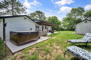 Un jardin avec un jacuzzi, un espace salon extérieur et une terrasse couverte.