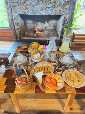 Una mesa de desayuno con diversos alimentos, un jarro de limonada y una chimenea al fondo.