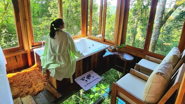 Una cabaña de madera con un ventanal grande, un lavabo, una mesita y un sofá.