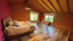 Un dormitorio de cabaña de madera con una cama, dos sillas, un ventanal y un radiador.