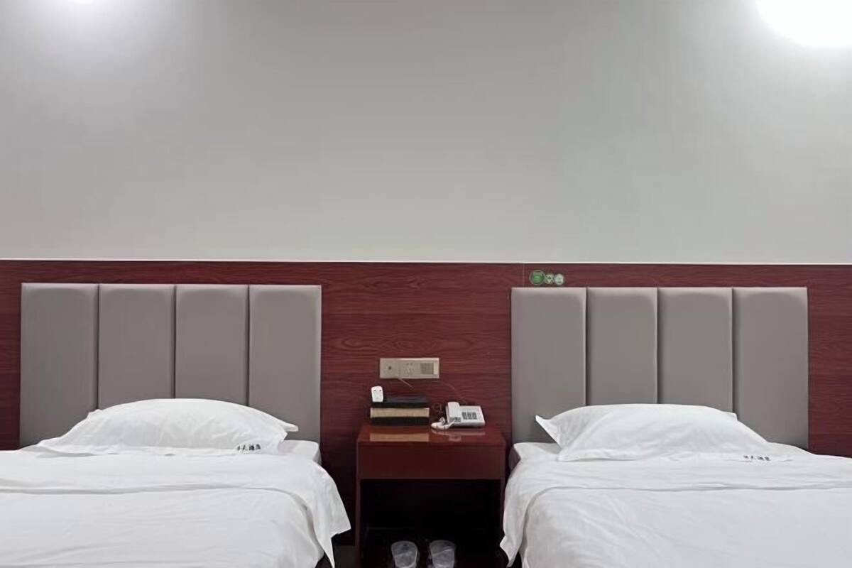 Ein Hotelzimmer mit zwei Betten, einem Nachttisch dazwischen und einem hölzernen Kopfteil.