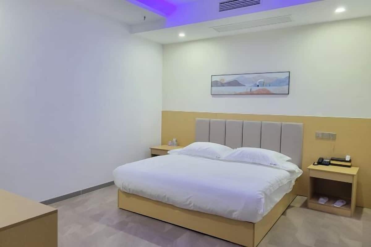 Ein Hotelzimmer mit Bett, Nachttischen, einem Wandbild und einer Deckenleuchte.