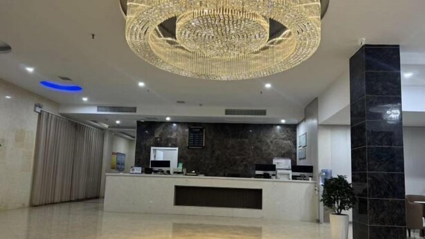 A modern reception area with a central desk, a large chandelier, and a potted plant.
