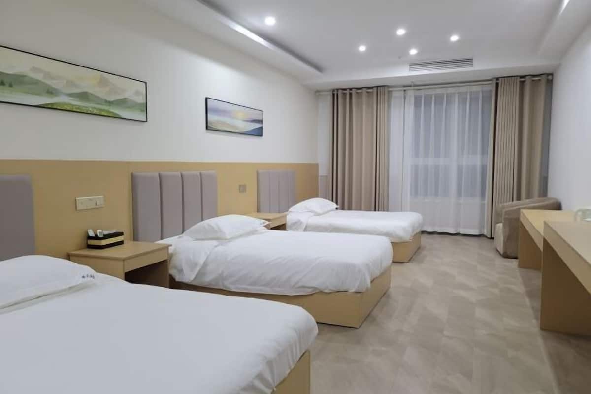 Ein Hotelzimmer mit drei Betten, einem Schreibtisch und einem großen Fenster mit Vorhängen.