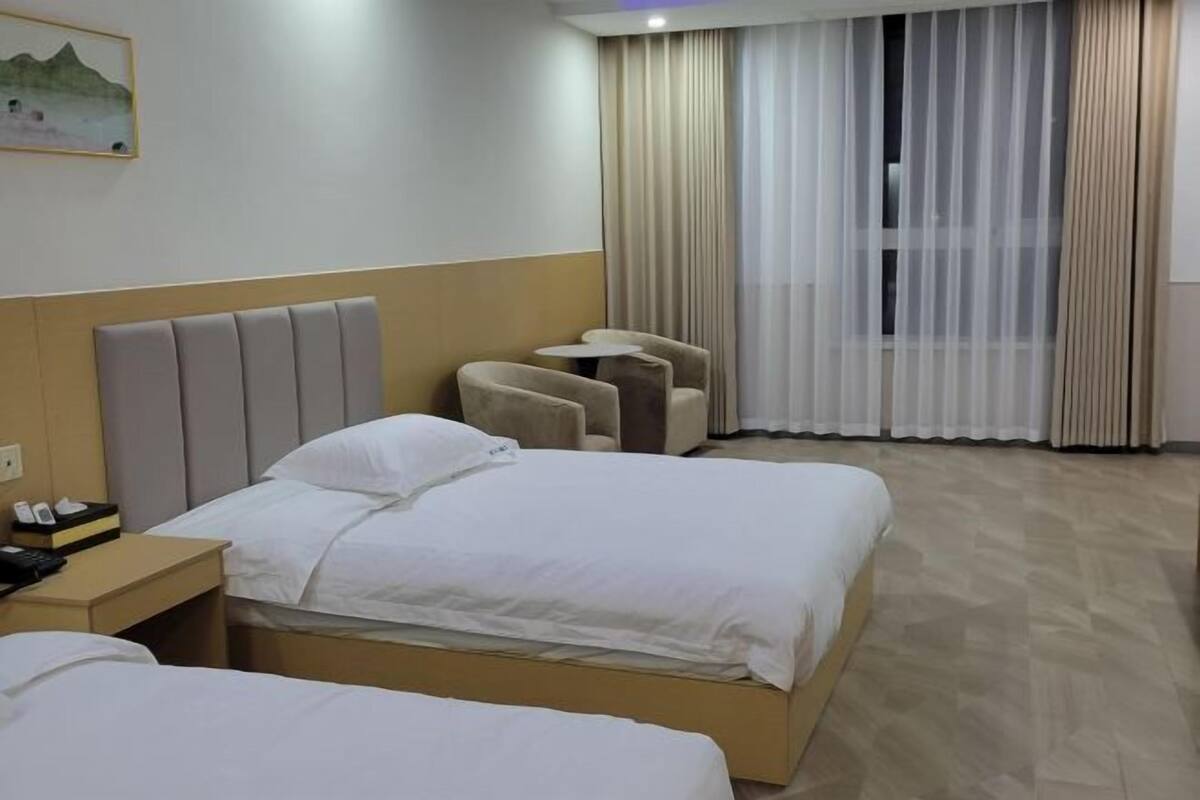 Ein Hotelzimmer mit zwei Betten, einem Kopfteil, einem kleinen Tisch mit einem Stuhl und einem Fenster mit Vorhängen.