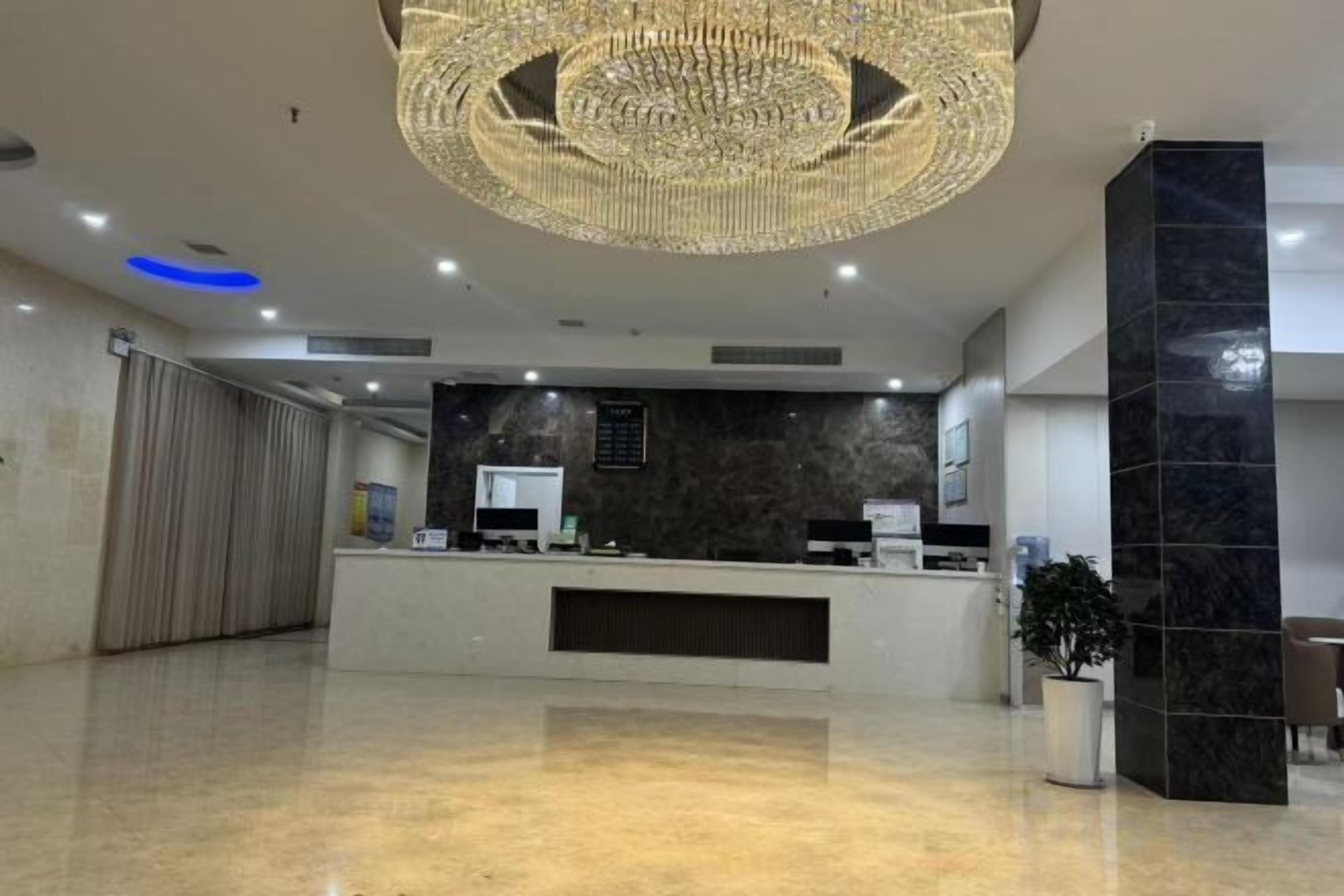 A hotel reception area with a modern chandelier, a reception desk, and a potted plant.