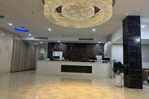 Zona de recepción de hotel con una lámpara araña moderna, un mostrador de recepción y una planta en maceta.