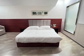 A modern hotel room with a large bed, a wooden headboard, a nightstand, and a large window providing a view.
