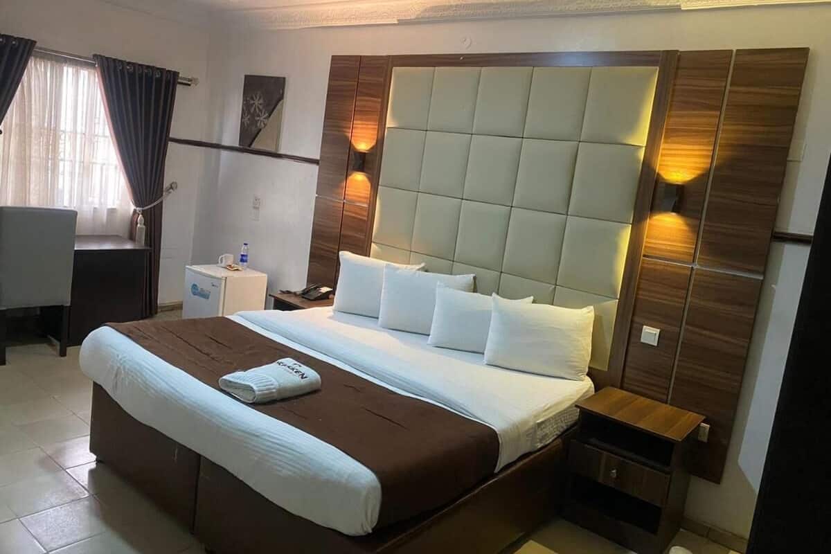 A hotel room with a large bed, a bedside table, a nightstand, a desk, and a chair.